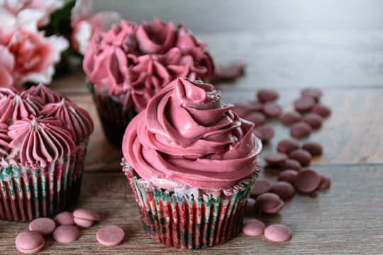 Closeup of three chocolate cupcakes with pink butter cream. Next to Ruby chocolate callets (with copy space).