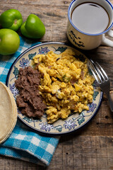 Scrambled eggs with green sauce and refried beans on wooden background. Mexican food