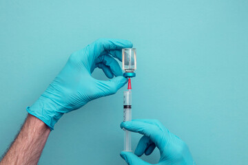 Doctor or nurse wearing blue surgical gloves holding a syringe and vaccine dose