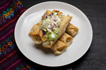 Fried tacos called flautas with guacamole and cabbage on dark background. Mexican food