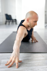 Fototapeta na wymiar Athlete bald man stretching body on fitness mat holding hands on the floor, concentrated on workout alone in studio. focus on hand