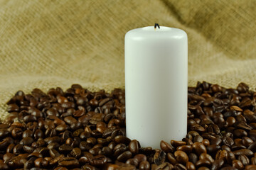 Mała, biała świeczka i ziarna niezmielonej kawy.