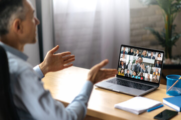A successful adult man uses a laptop for video communication with business partners. A manager or ceo is sitting at his desk, talking on a video call with colleagues, successful employees are on the