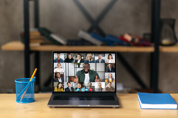 Online business briefing, brainstorm. A laptop stands on the desktop, on the laptop screen is many different multiracial coworkers, gathered, communication, solving working issues