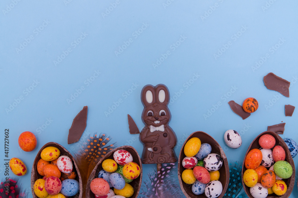 Wall mural Flat lay Easter eggs hunt sweets concept with chocolate bunny and eggs on blue background copy space