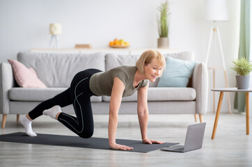 Online sports during home isolation. Fit mature lady doing exercises in front of laptop indoors,...