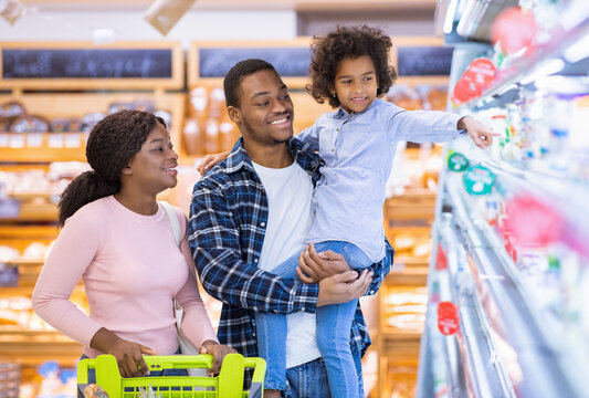 Happy black parents and their pretty daughter with shopping cart having fun buying groceries at hypermarket