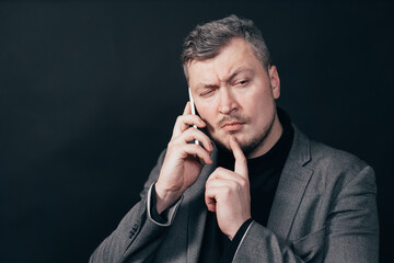 Man standing with hand on chin thinking about question during phone call, pensive expression. Thoughtful face. Doubt, hard decision, important information concept.