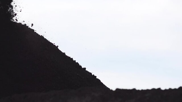Slow Motion Close Up Shot of Coal falling into a Large Pile of Coal at a Coal Mine framed far left in North America stock footage