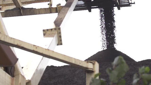 Slow Motion Medium Shot of Coal falling into a Large Pile of Coal at a Coal Mine framed right in front of swaying plant in North America stock footage