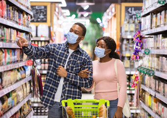 Millennial black couple in face masks shopping at grocery department of supermarket