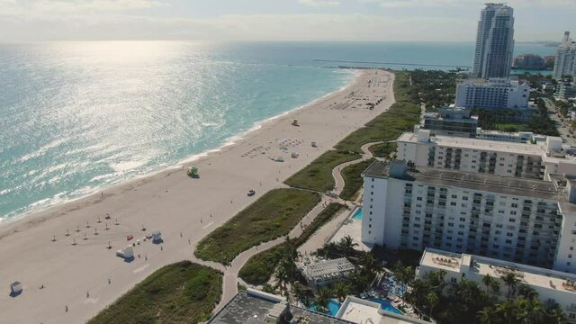 Sunlight Reflection On Blue Ocean With Modern Luxury Hotels At Mid-Beach Area In Miami Beach, Florida, USA. - Aerial Tilt-Down Shot