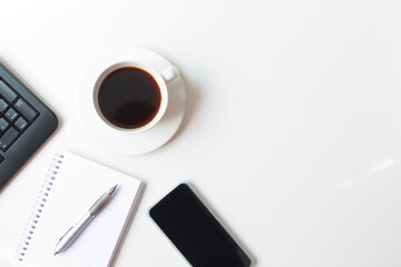 A white cup with black coffee, a mobile phone and a notebook with a pen and keyboard are on a white background. Business theme. A set of office utensils. Free space for text. View from the top point.