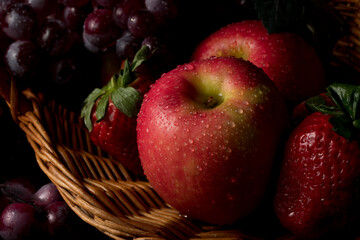 Fruit basket still life with fresh fruits in a wicker basket on black background with copy space