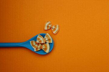 White-orange farfalle paste in a blue spoon on an orange background. Farfalle striped pasta.