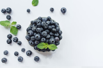 Fresh blueberries in white bowl and green leaves on white background. Flat lay, top view, copy space