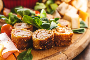 Close up on cheese and ham rolls on the wooden board plate with various food and cheese ready to eat - appetizer on the table full frame