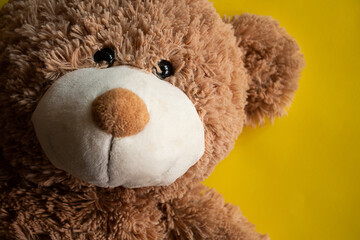 Happy and cute teddy bear with a smile over a yellow background; toy for a happy child. Close up...