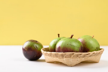 Ripe purple and green star apple fruit in a bamboo basket on white and yellow background, Tropical fruit