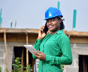 A Nigerian female construction and architectural engineer with blue safety helmet happily talking on phone 