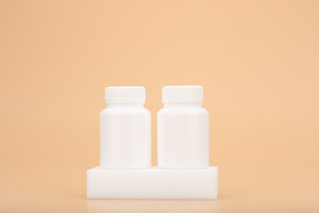 Two white medication unbranded bottles on white podium against beige background with copy space. Concept of vitamins, mineral supplement, healthy lifestyle and wellbeing