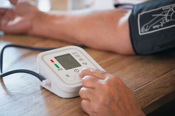 Senior woman is checking blood pressure and heart rate with digital pressure gauge by herself at...