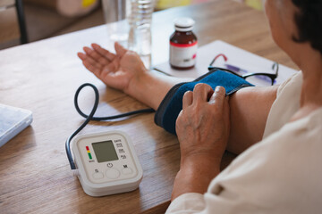 Senior woman is checking blood pressure and heart rate with digital pressure gauge by herself at...