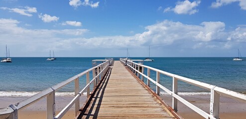 Obraz premium Wooden white bridge to the sea with dramatic sky view over the long jetty in Hervey Bay Australia