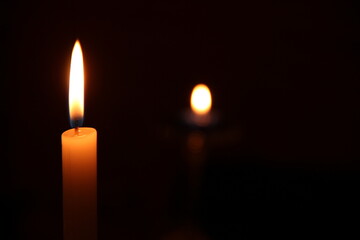 Candle lit ahead, in the dark, with another candle in the black background, yellow tone, bokeh. Candle in the dark, Design for the background.