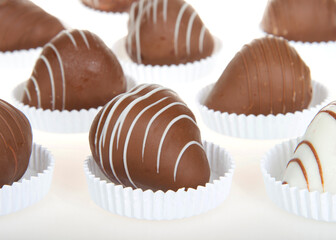 Close up on giant strawberries dipped completely in white and milk chocolate, drizzled with contrasting white and milk chocolate. sitting in shallow white paper pastry dishes on reflective surface