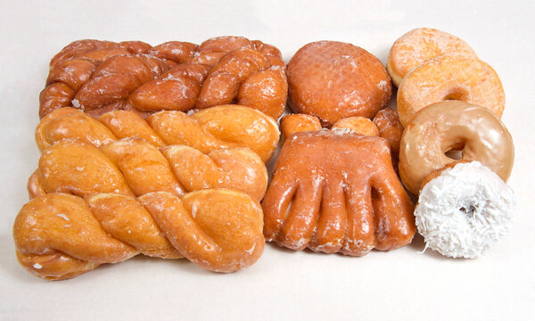 Variety of donuts arranged on parchment paper clustered together. Bear Claw, glazed twists, Cinnamon Twist, jelly filled, sugar coated, coconut covered.