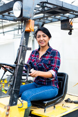 Confident hispanic woman working at the company sits behind the wheel of a forklift truck.