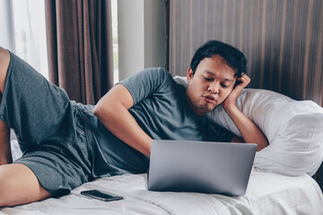 Young Asian man is sad and angry when playing a game in laptop and phone at bed