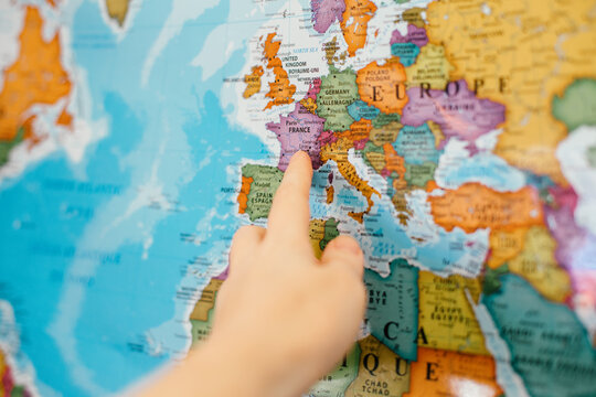 Human woman man hand pointing out to Europe country on map. Travel dream destination. France country landmark on a world global colorful map. Dreaming about travelling and crossing borders. - Powered by Adobe