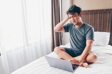 Young asian Man with a laptop in bed is confused and stress. Work from home concept