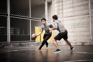 two young asian men playing basketball outdoors