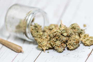 Medical cannabis flower buds in small clear jar on white wood background.
