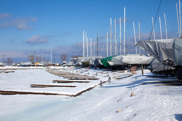 Sailboats line the perimeter of the Thornbury Yacht Club during the winter months when the harbor is frozen. The boats are winterized and covered up. The marina is frozen and the docks snowy.