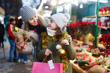 Smiling girl with woman are buying Christmas ornamentals in the market outdoor.