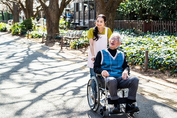 楽しそうに外を散歩する車椅子に乗った高齢者と散女性福祉士