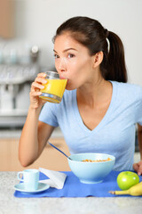 Breakfast at home Asian woman drinking fresh cold pressed orange juice beverage during cereal meal in kitchen. Vertical portrait.