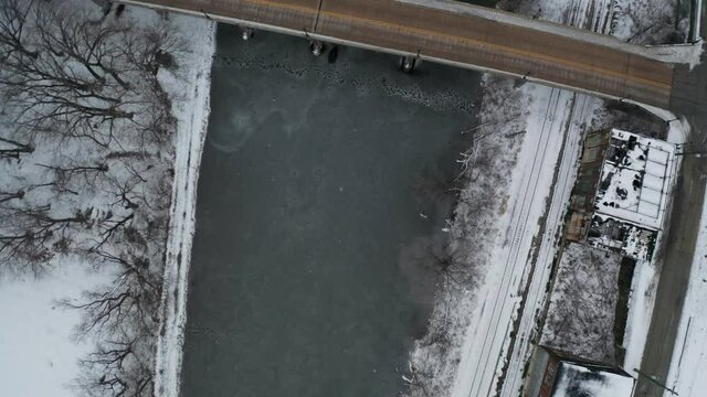 Top down aerial view of frozen river and small road bridge in urban area