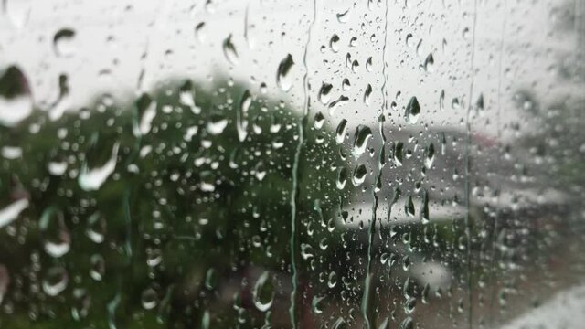 Close up of rain droplets falling down on window glass moisture surface, heavy rain shower outside condense window