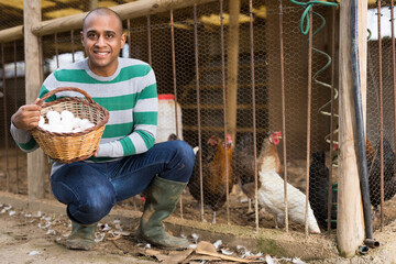 Smiling male farmer at a poultry farm holds a basket of chicken eggs . © JackF
