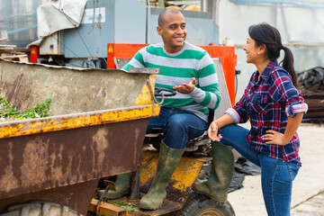 Couple of male and female hispanic workers talking and discussing something near forklift loader at...