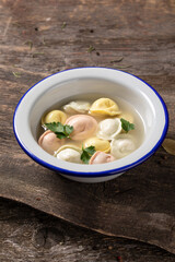 Traditional Russian dumplings made from multi-colored dough in broth. Dumplings on a wooden board in an enamel plate. Cooking concept.
