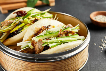 Bao bun with roast duck. Bamboo steamer on dark slate table. Chinese, asian, authentic food concept