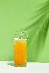 Mango lemonade drink over green background. White table with sunlight and palm leaf hard shadow. Summer, tropical and juicy concept