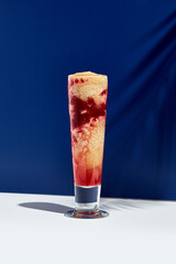 Raspberry and banana smoothie over white and blue background. Palm leaf with sunshine and hard shadow. Fruit yogurt or shake drink in high glass. Summer, healthy, fresh drink concept
