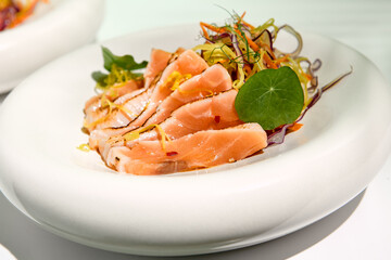 Salmon tataki in sesame with salad. Fish sashimi restaurant appetizer on white table with green wall. Day sunlight with hard shadow of tropical palm leaves. Summer or spring food concept.